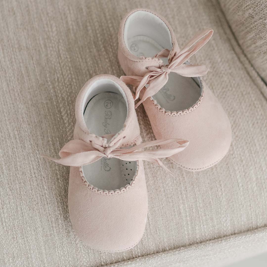 Top-down view of the Lola Suede Tie Mary Janes. The baby shoes are crafted from rosy pink suede with scalloped edge detailing and tied with soft cotton ribbon bows.