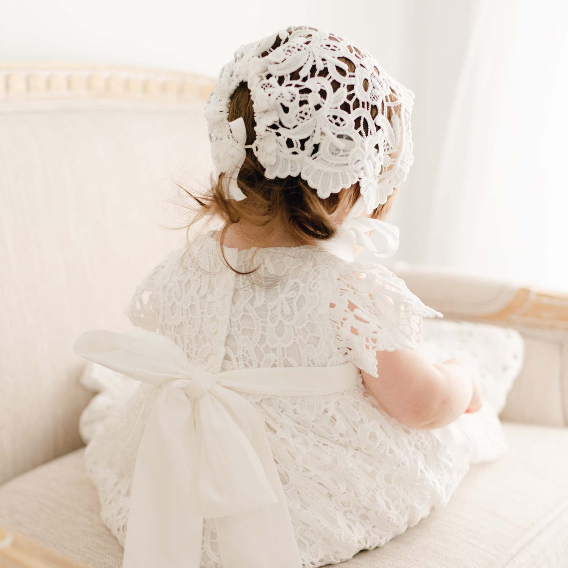 Back detail of the Lola Christening Gown and Bonnet, worn by a baby girl. The gown features back ties, a cotton sash, and a button closure