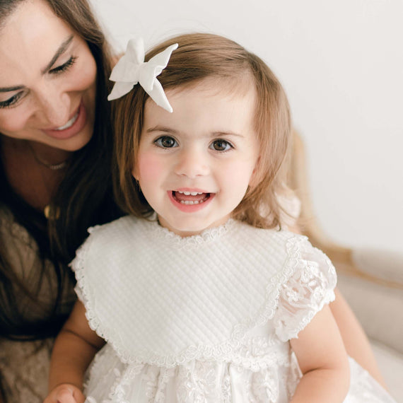 baby girl smiling with mom and a baptism bib.