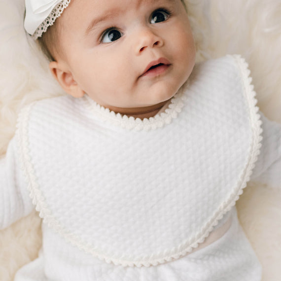 Newborn baby girl wearing the Tessa Quilt Bib made with a soft quilted cotton and accented with a floral edge lace.