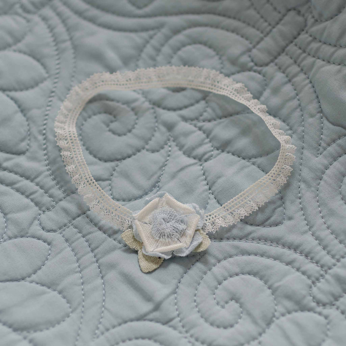 Flat lay of the Petite Fleur Linen Flower Headband on a quilted blue blanket, featuring a delicate lace band and a light blue linen flower accent.