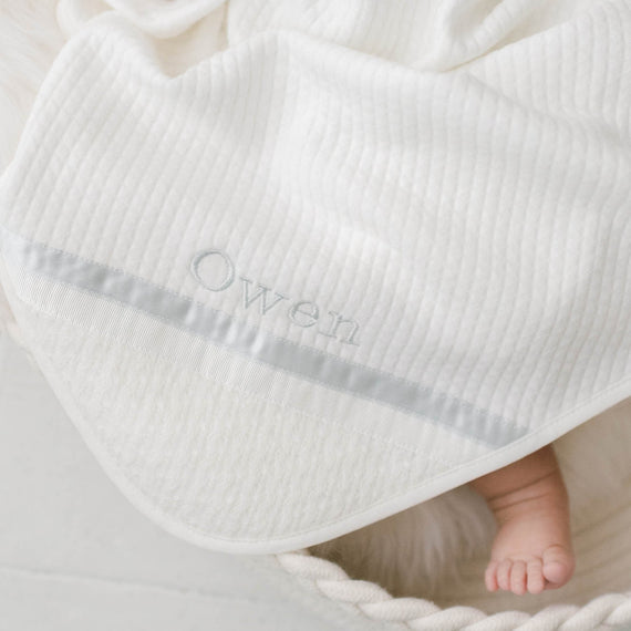 Photo of the corner of the Owen Personalized Blanket. The corner features an ivory knit and the name "Owen" embroidered with light blue thread