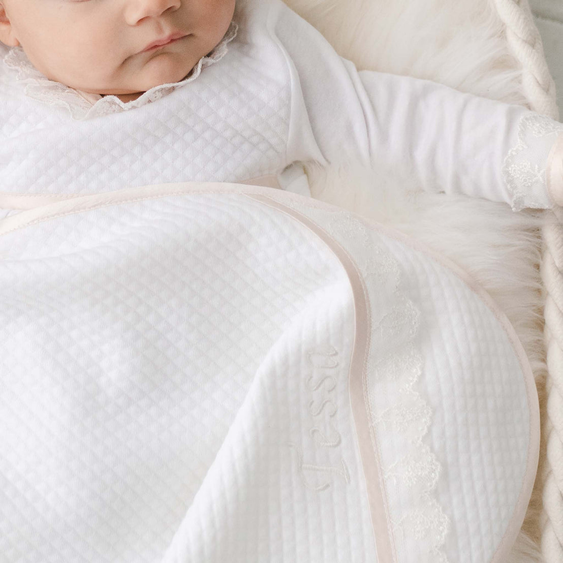 Close up photo of the Tessa Personalized Blanket. The blanket is made from soft textured cotton with the corner of the blanket featuring a ivory embroidered lace trim and personalized name embroidery.