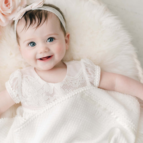 Baby girl smiling, snuggled in the Victoria quilted cotton blanket.