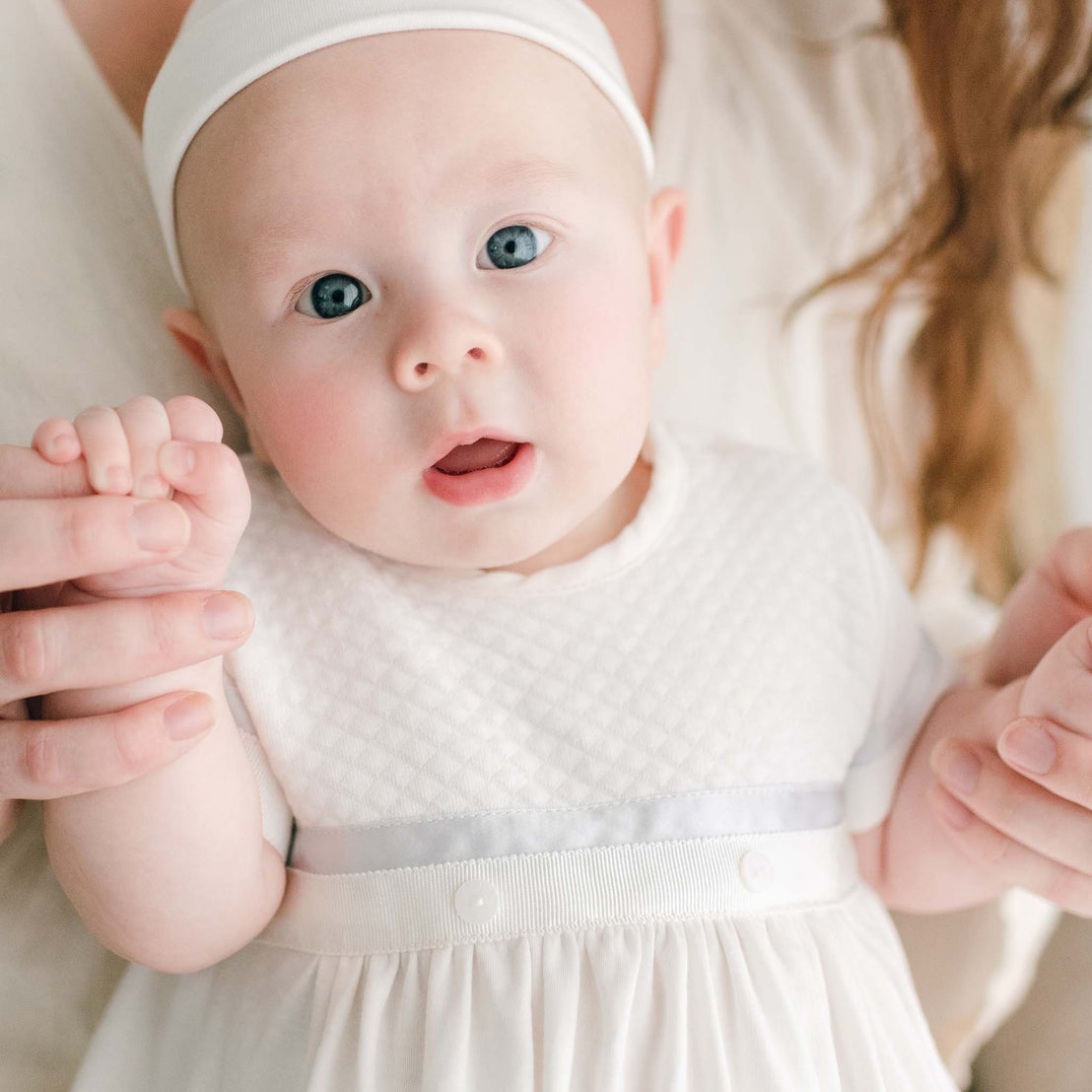 Close up photo of baby boy sitting on his mother's lap. He is wearing the Owen Layette and Knot Cap