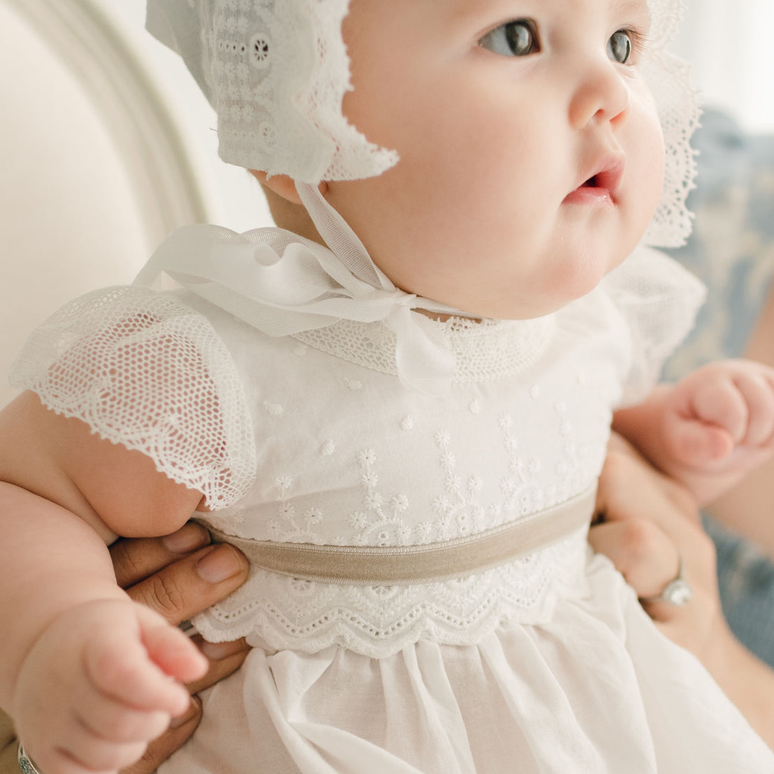 Detail of the Emily Gown bodice with tan sash tie. The Emily Gown features embroidered cotton eyelet lace with a scalloped edge, lace trim and soft lace cap sleeves.