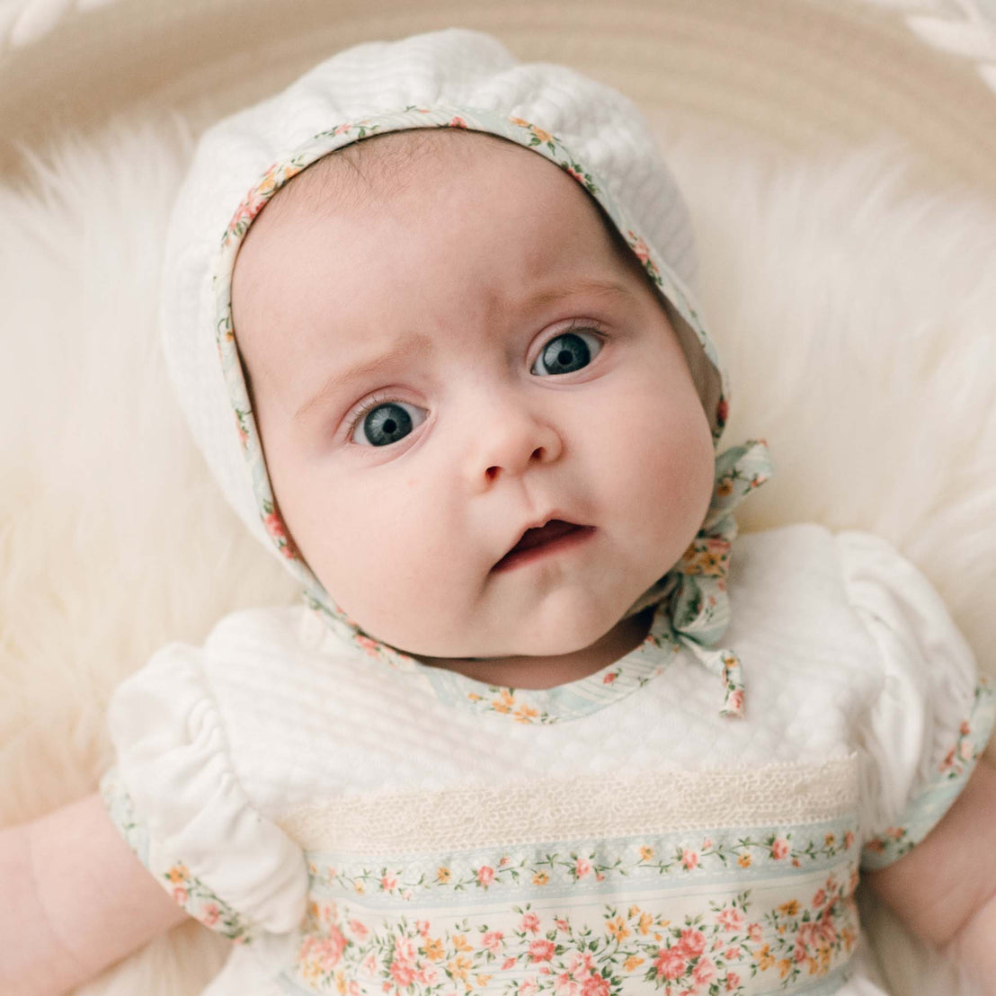 Newborn baby girl wearing the "Powder Blue" color Eloise Layette Gown with matching Eloise Quilted Bonnet. Perfect for a formal baby outfit.