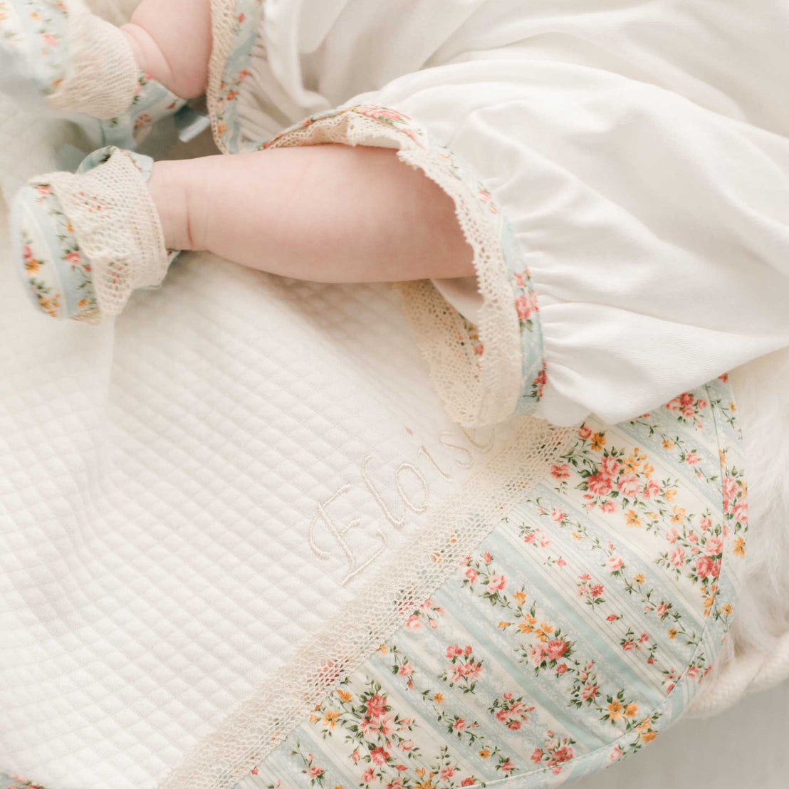 Corner detail of the "Powder" Eloise Personalized Blanket. Crafted with soft plush quilted cotton. One corner of the blanket features the Eloise cotton floral pattern. A personalized name can be embroidered on the corner as well in champagne thread.