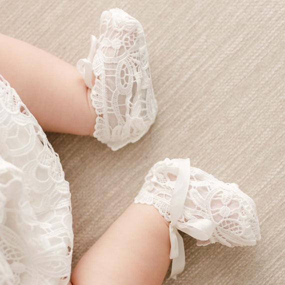 Close-up of a baby wearing Lola Booties, featuring light ivory lace and silk bow ties, with lace details matching the baby’s outfit.