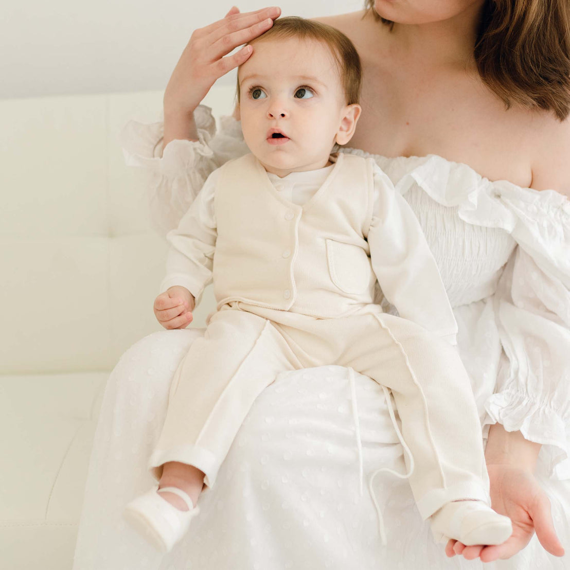 Baby boy sitting on his mother's lap. He is wearing the Braden Vest Shorts Suit made of ivory French Terry