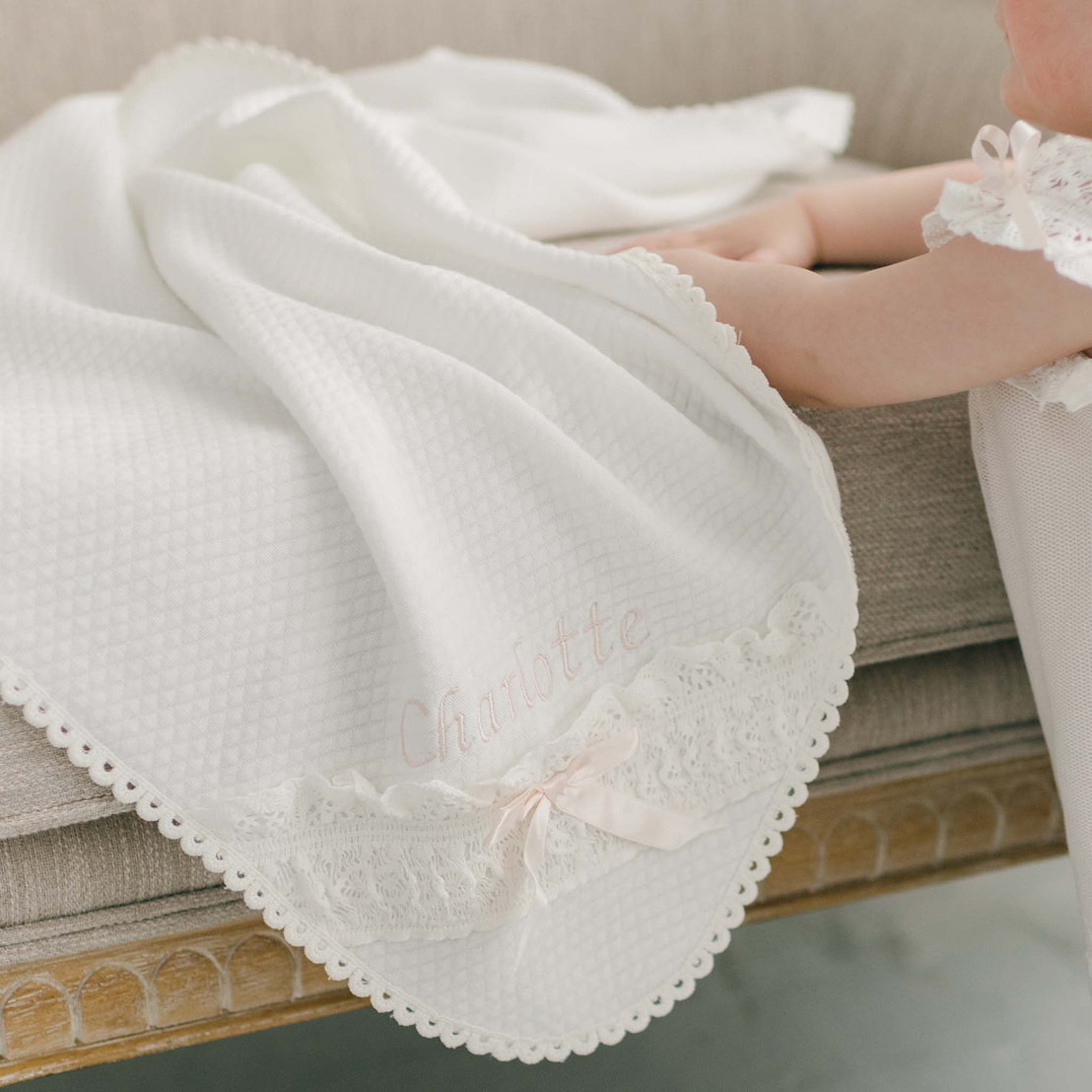 Close-up of a delicate vintage white lace fabric with a pink bow detail, highlighting intricate patterns and textures on a light background, suitable for christening or baptism ceremonies.