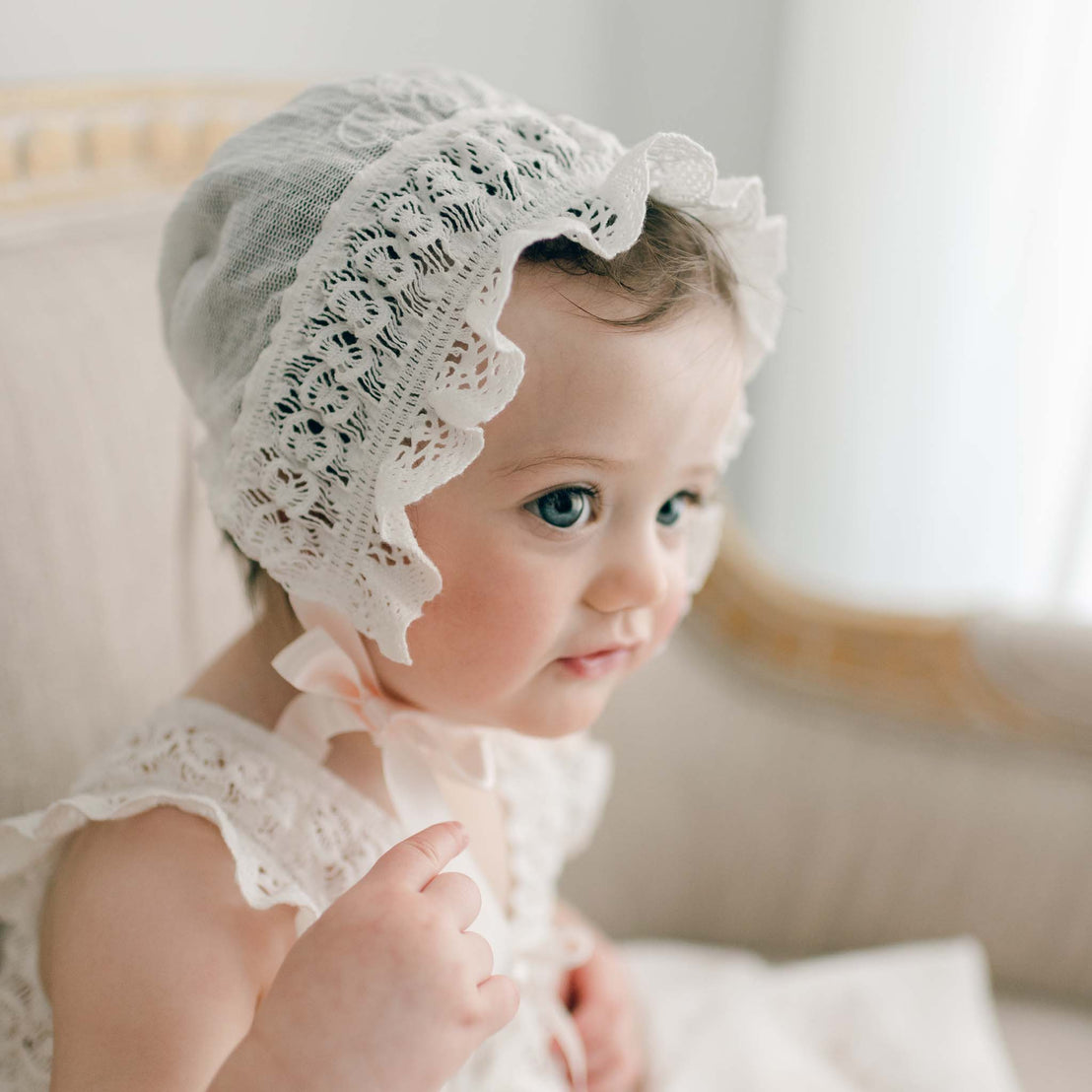 Close-up of a baby girl wearing the Charlotte Christening Gown & Bonnet with rose and vine embroidery, focusing on the texture of the cotton lace.