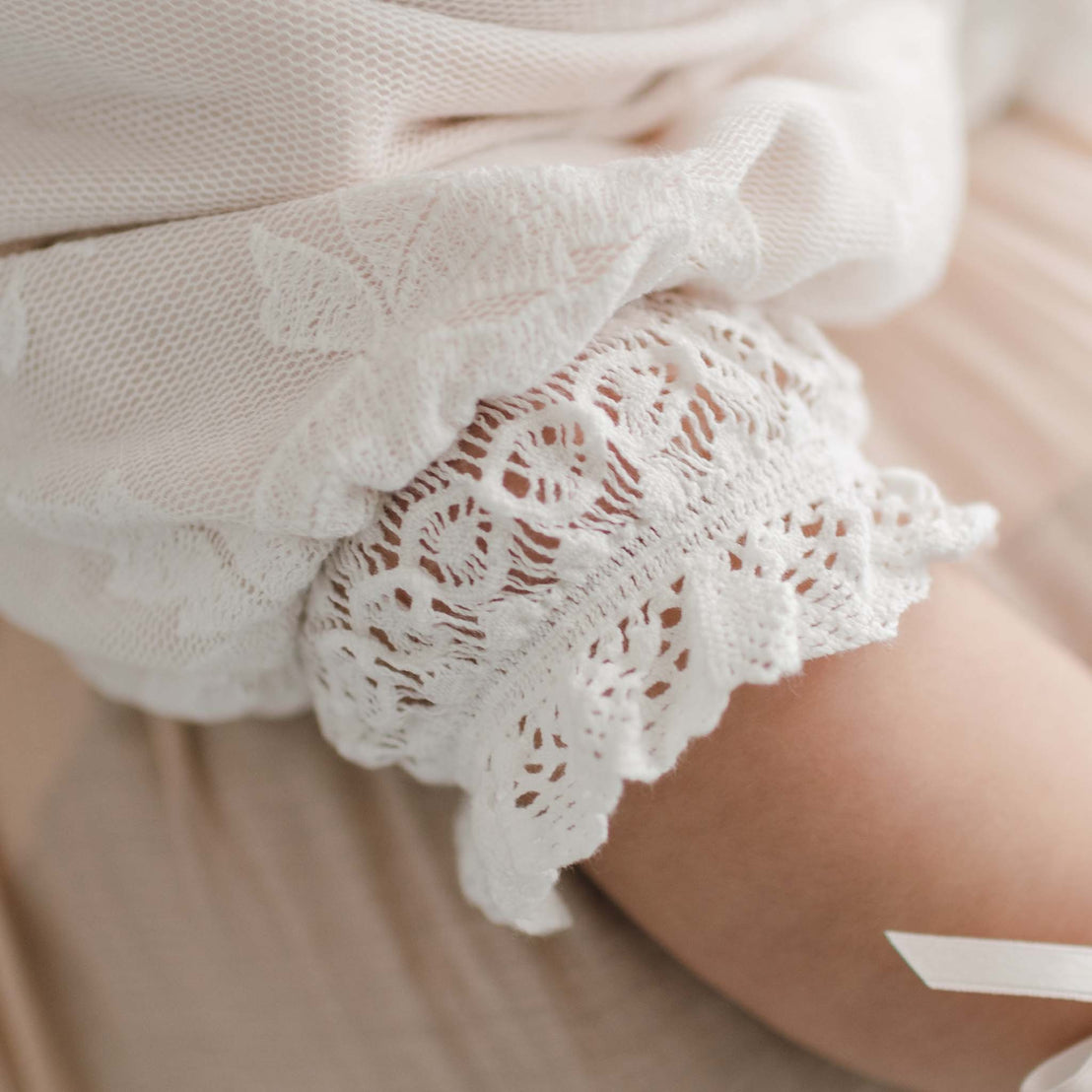 Close-up of the hem on the Charlotte Romper as featured on a baby girl. The romper is made with intricate embroidered cotton lace trimming.