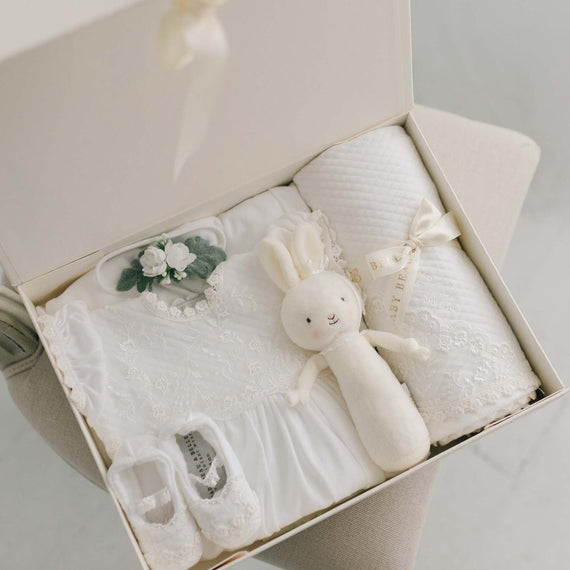 The Ella Newborn Gift Set, showcased in a white gift box, includes the Ella Layette Gown, matching Ella Booties and a Petite Flower Headband, along with a bunny chime rattle and coordinating blanket.