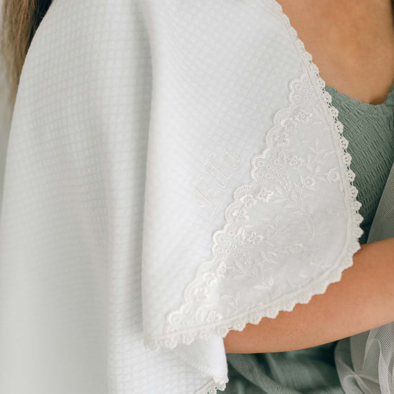 A close-up of a person's shoulder draped in the Ella Personalized Blanket, featuring intricate floral lace trim and the personalized embroidered name 'Ella.'