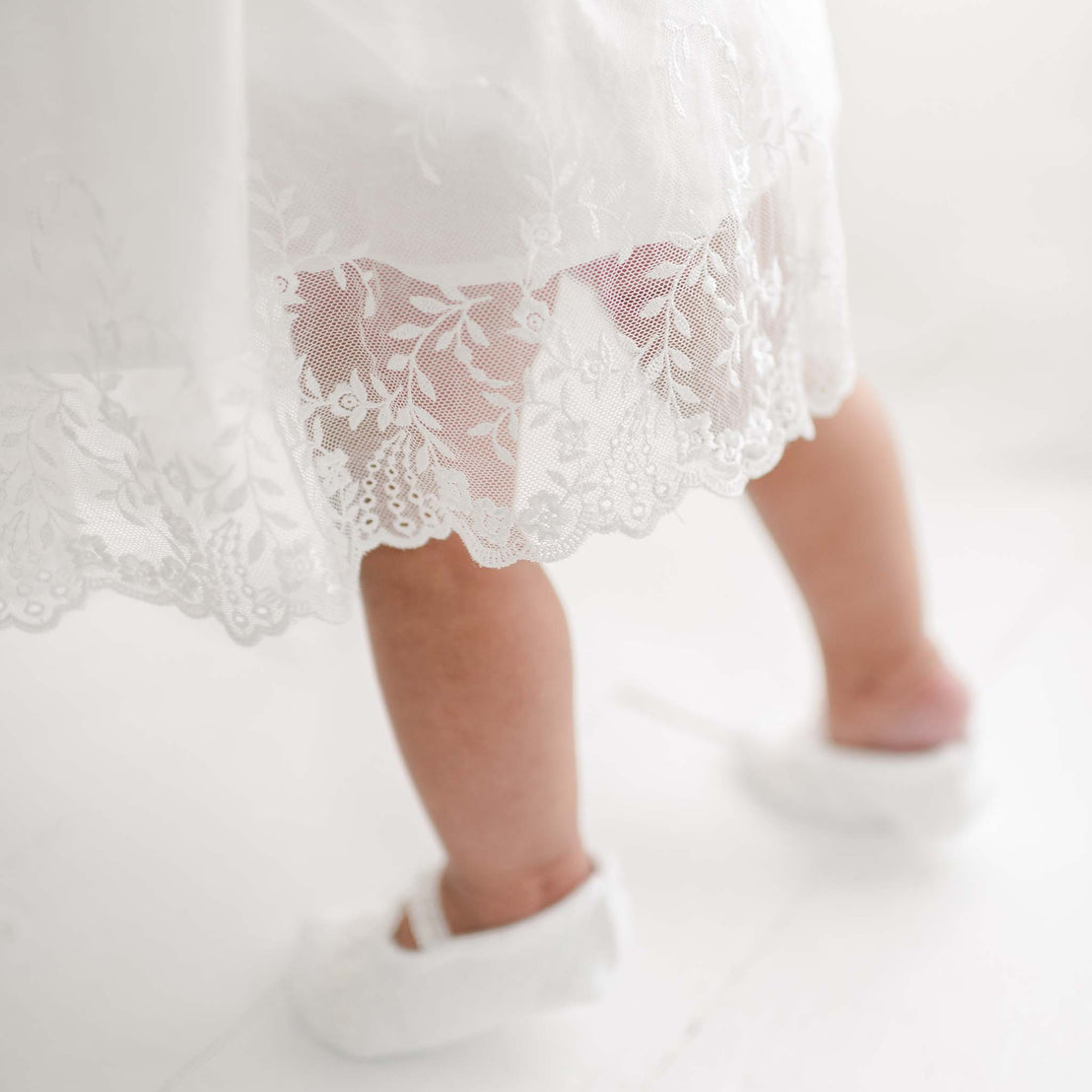 Close-up of a toddler's legs standing in the Ella Booties and Ella Romper Dress, showcasing the delicate floral embroidered netting lace.