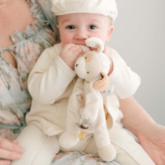 Baby boy wearing the Ezra Tan 4-Piece Suit and holding an Ezra Tan Silly Puppy Buddy stuffed animal that serves as a pacifier holder