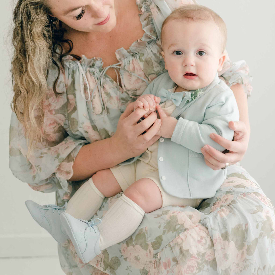 Baby boy sitting on his mother's lap. He is wearing the Ezra 4-Piece Powder Blue Suit, blue velvet bow tie and boutonniere