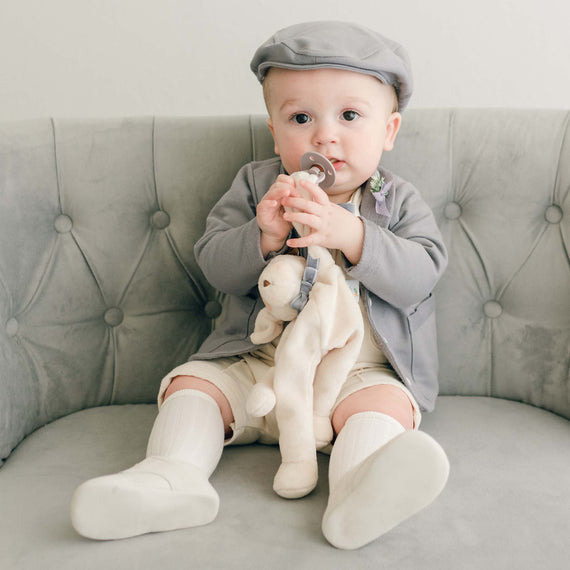 Baby boy wearing the Ezra 4-Piece Suit and holding an Ezra Heather Silly Puppy Buddy stuffed animal that serves as a pacifier holder