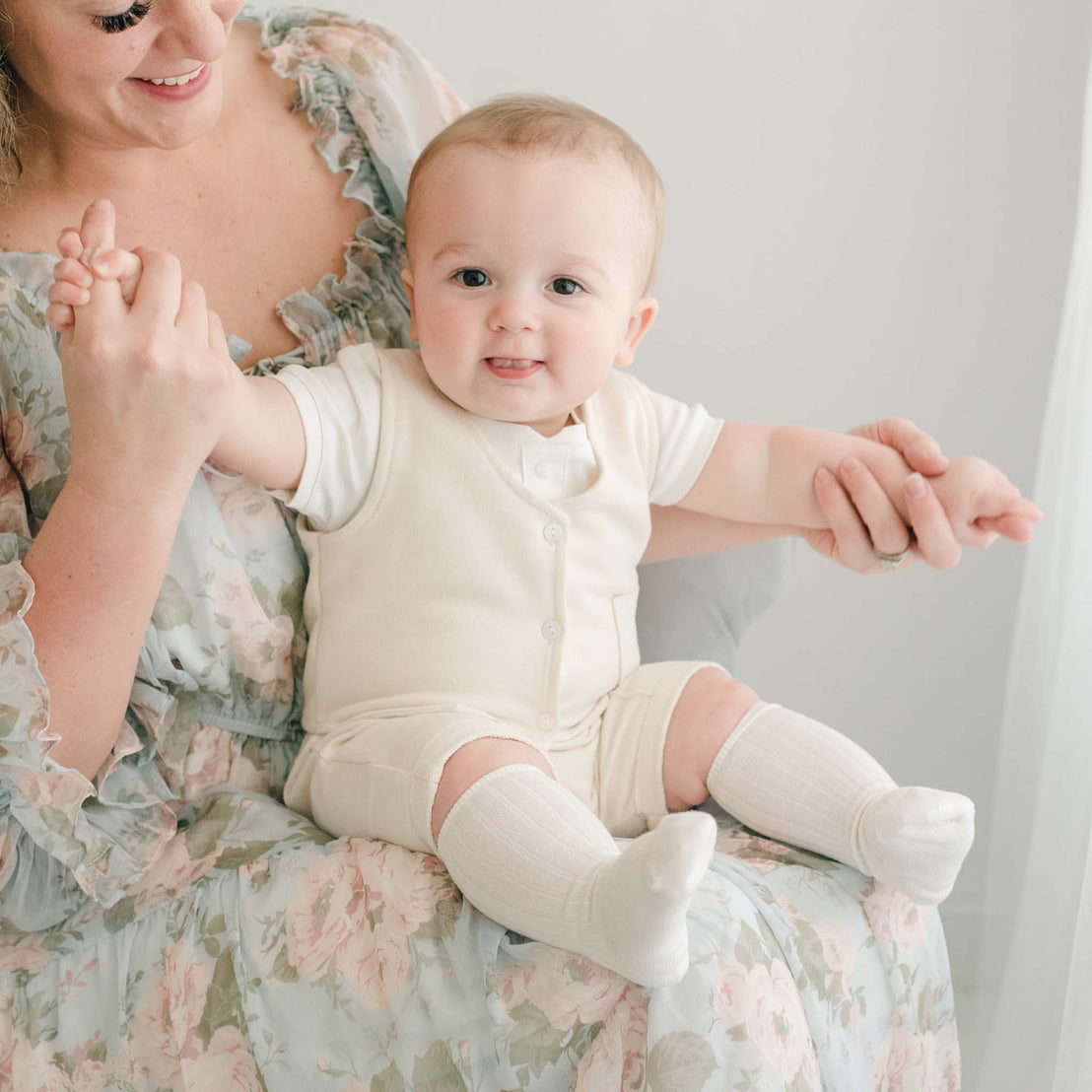 Baby boy sitting on his mother's lap. He is wearing the Ezra Beige Vest, Shorts, and knee-high socks