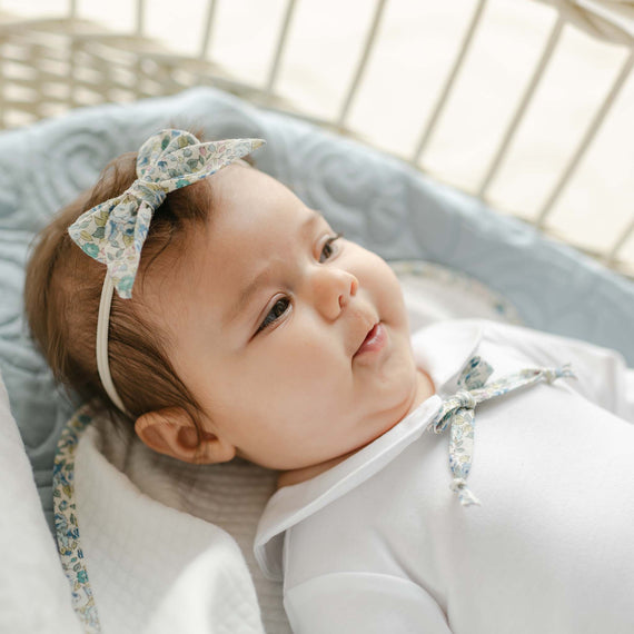 Baby lying on a quilted surface wearing the Petite Fleur Bow Headband, featuring a floral bow on a soft nylon band.