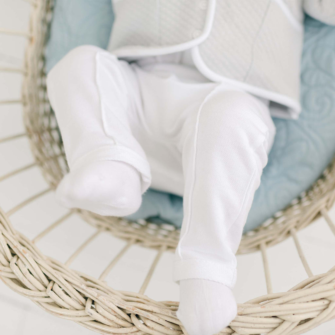 A baby dressed in the Grayson 3-Piece Suit is lying in a woven basket with a blue quilted blanket. The focus is on the Grayson Pants with pleated front creases.