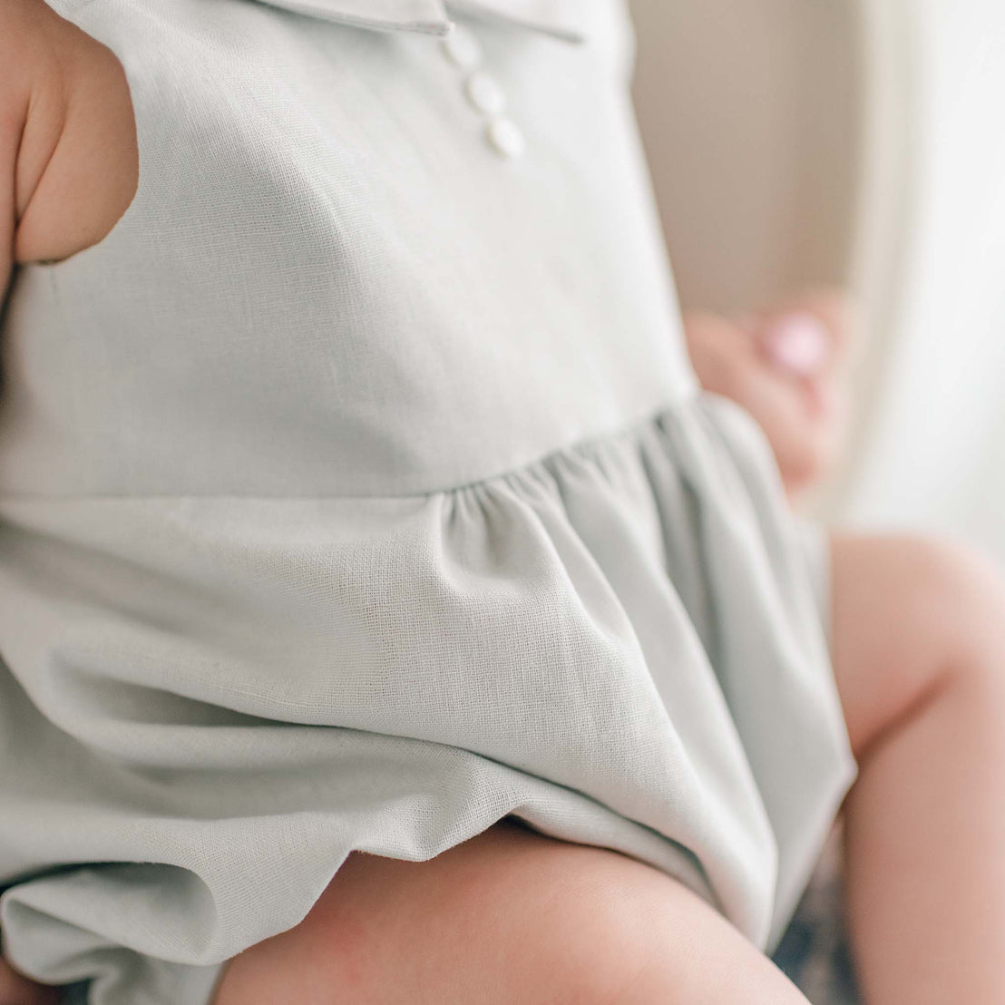 A close-up of a baby wearing the Owen Linen Romper. The background is softly blurred.