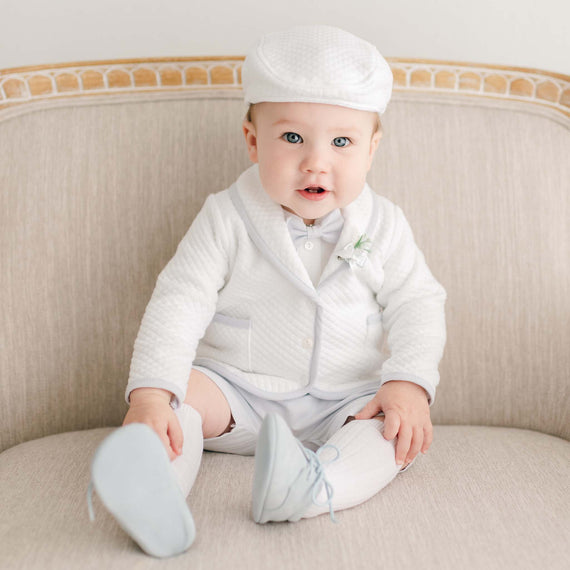 Baby boy sitting on a chair wearing the Harrison 3-Piece Shorts Suit made with plush white quilted cotton jacket, hat, and light blue shorts 