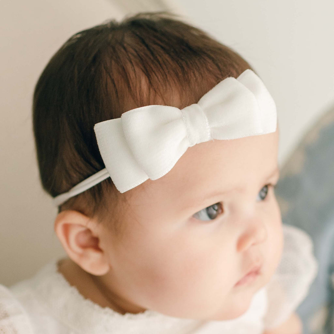 A newborn baby girl wearing the Ella Baby Girl Bow in Velvet looks away from the camera.