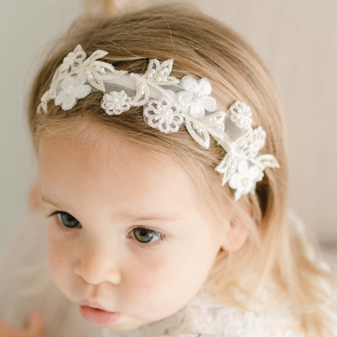 Close-up of a toddler girl wearing the Lola Beaded Flower Headband, highlighting the velvet band with intricate pastel pink and ivory floral accents.