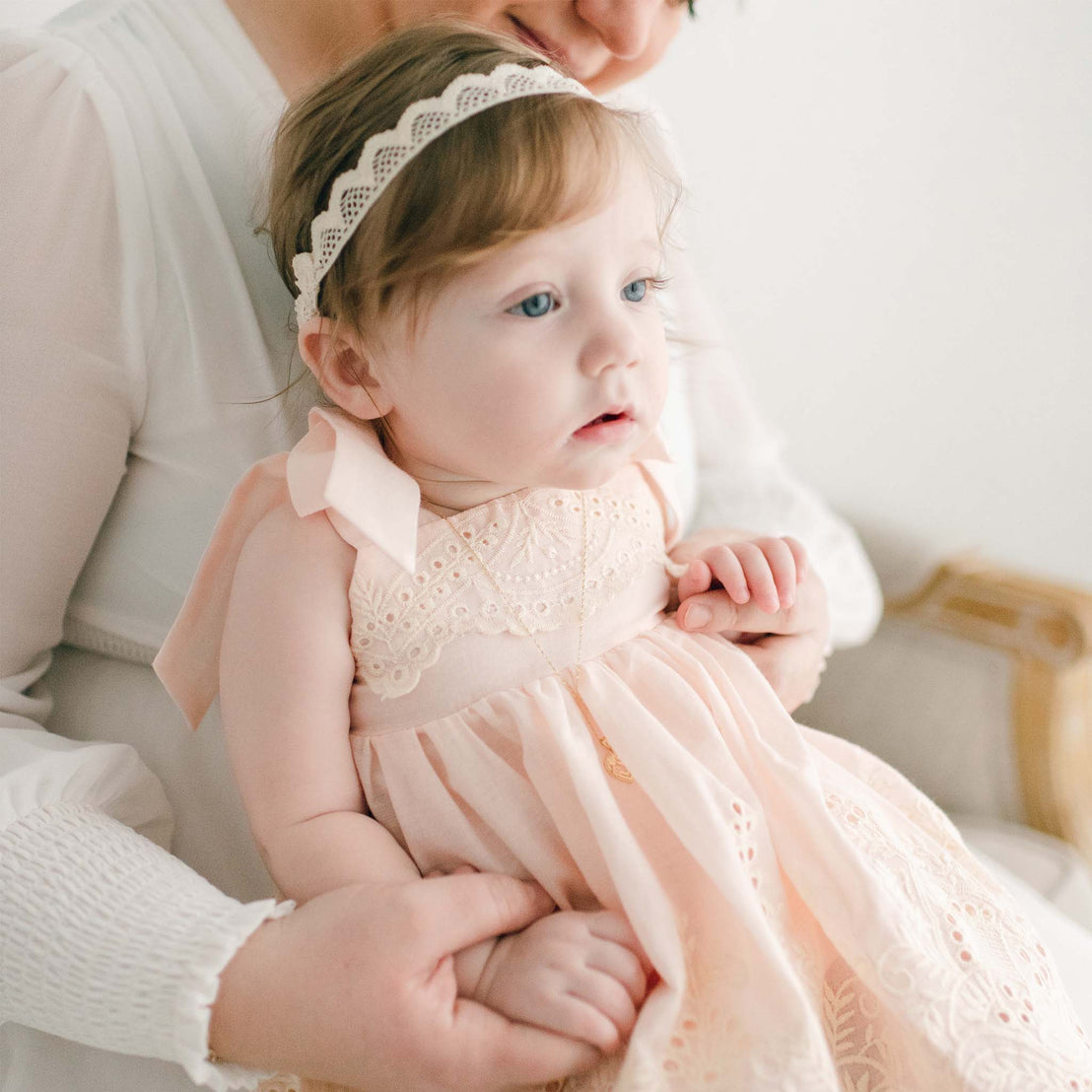 Baby girl sitting on her mother's lap and wearing a pink Ingrid Romper Dress and lace headband