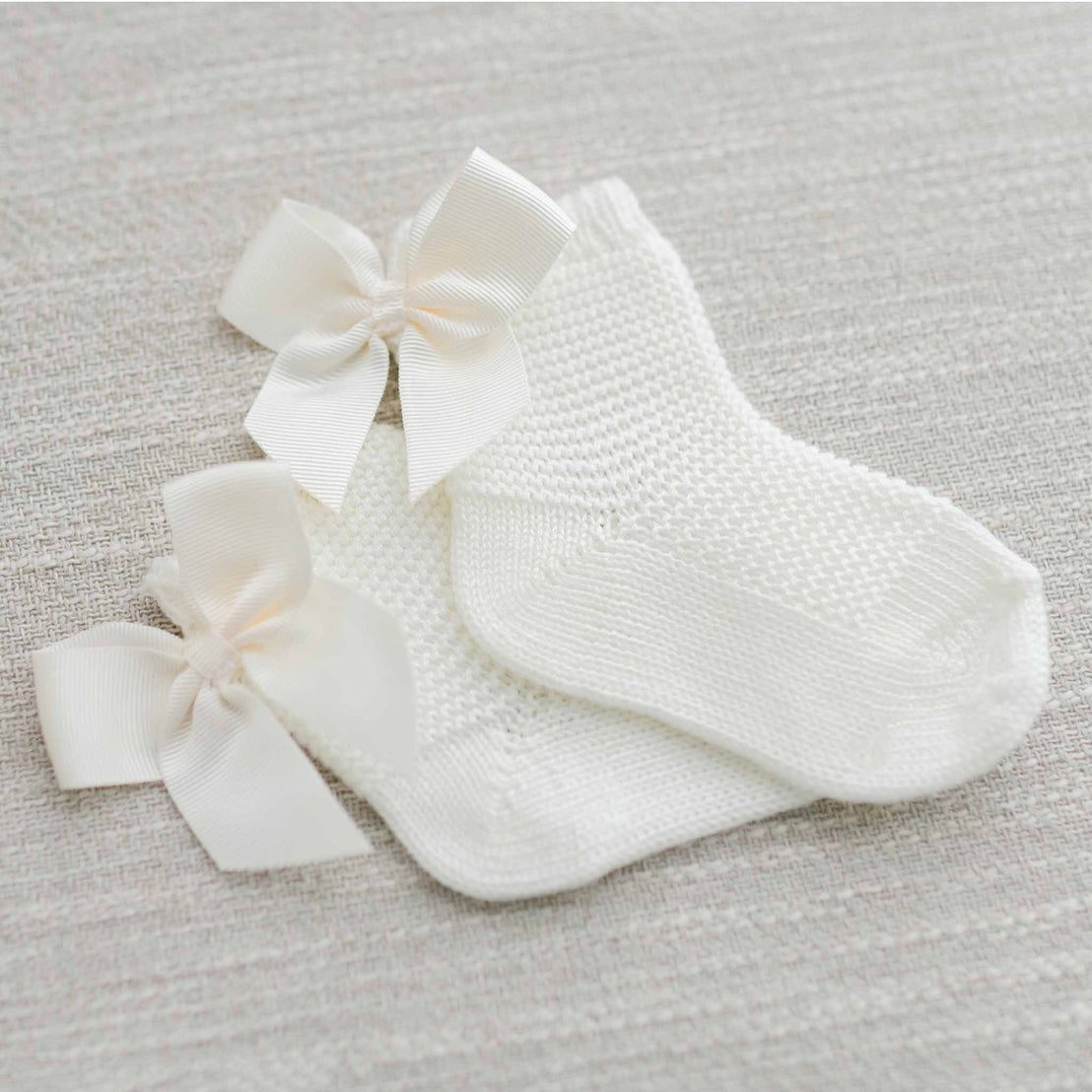 A pair of Garter Stitch Socks with Bow in ivory presented on a soft-textured light gray background.