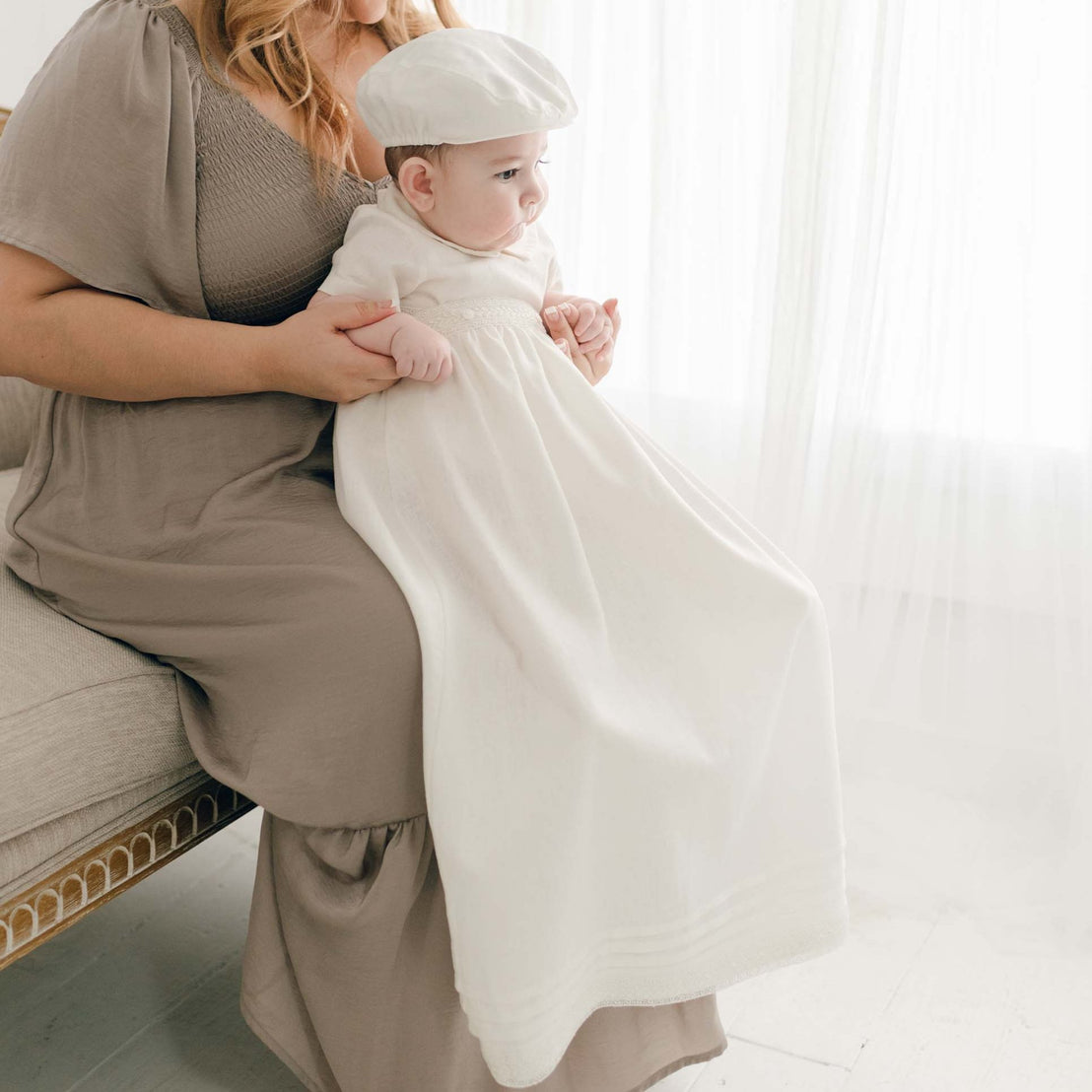 Baby boy wearing the convertible baptism gown and Romper Skirt Set. The skirt attaches to the Oliver Romper to turn the romper into a traditional christening gown. He is also wearing the Oliver Linen newsboy Cap.