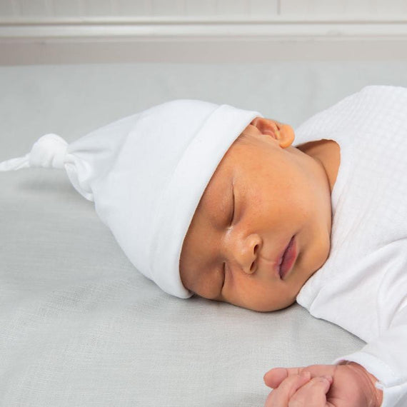 A newborn baby wearing the Elijah Newborn Knot Cap made with soft pima cotton in white and featuring a knot design