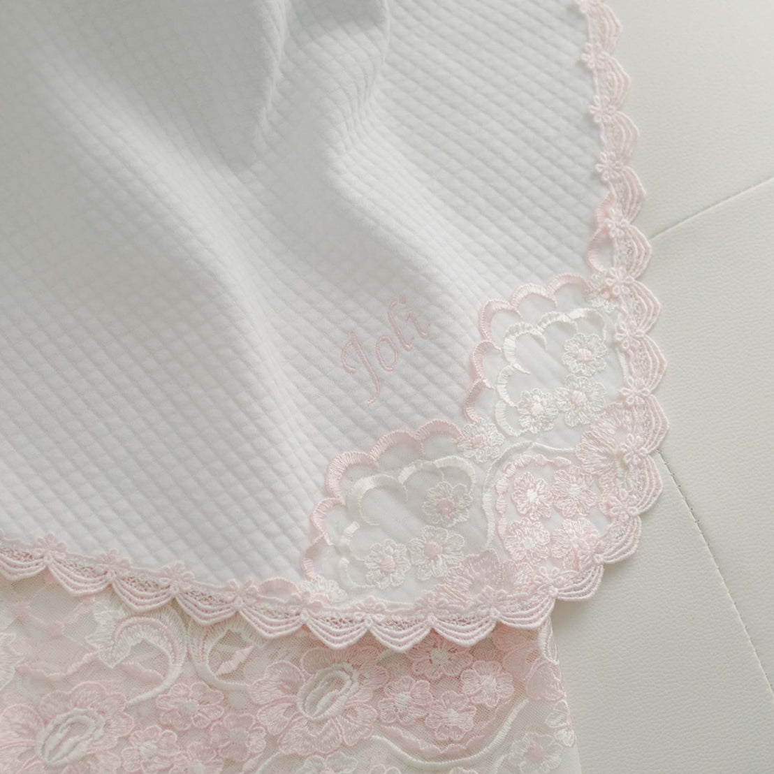 Close-up of a Joli Blanket with delicate lace detailing and the word "Joli" embroidered in a light thread, perfect for a boutique or baptism.