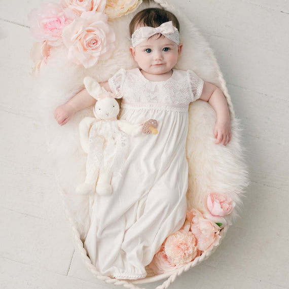 Baby girl with smile laying down in a basket wearing the traditional cotton layette gown. Part of our Victoria Christening Collection.