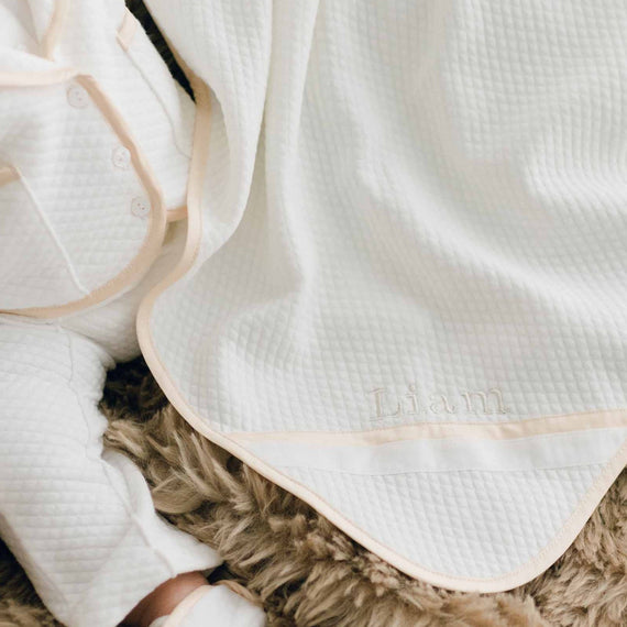 Photo of a baby sitting on a brown fur blanket. The baby is wearing the Liam 3-Piece Suit and is covered with the Liam Personalized Blanket