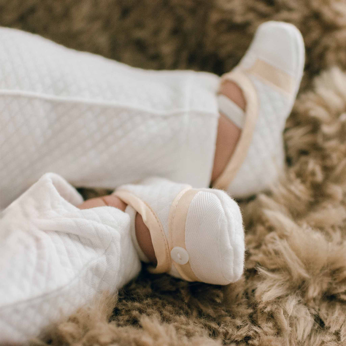 Boy wearing a pair of the Liam Booties made from soft quilted cotton with a champagne silk trim and accented with cotton ribbon and buttons on the toe. A soft elastic strap helps keep them on his feet