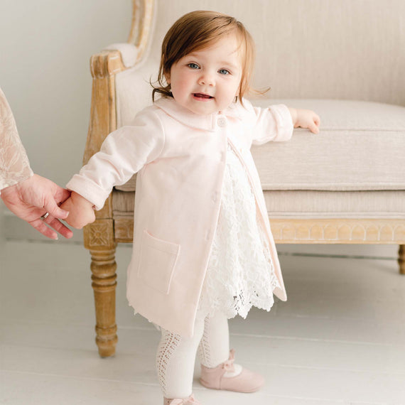 Baby girl wearing the Lola Trench Coat over the Lola Bubble Romper. The soft pink coat is made from cotton French terry and features a petite collar, button closures, and front pockets.