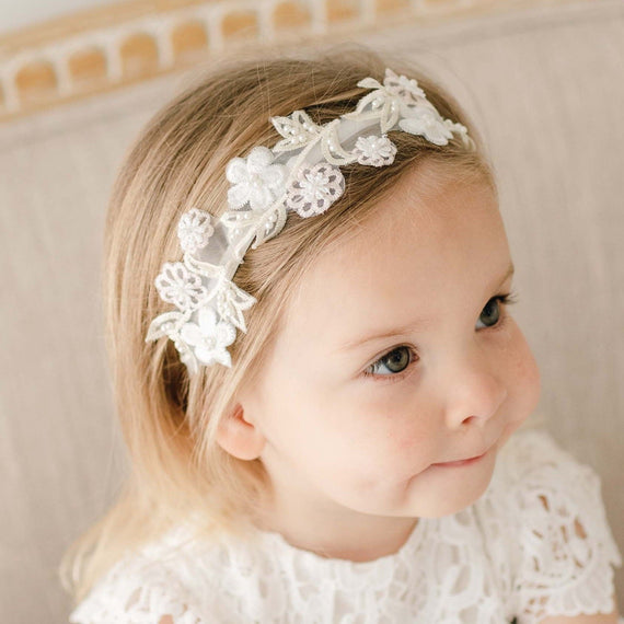 Toddler girl wearing the Lola Beaded Flower Headband, featuring a velvet elastic band with pastel pink and ivory floral appliqué, looking to the side with puckered lips.