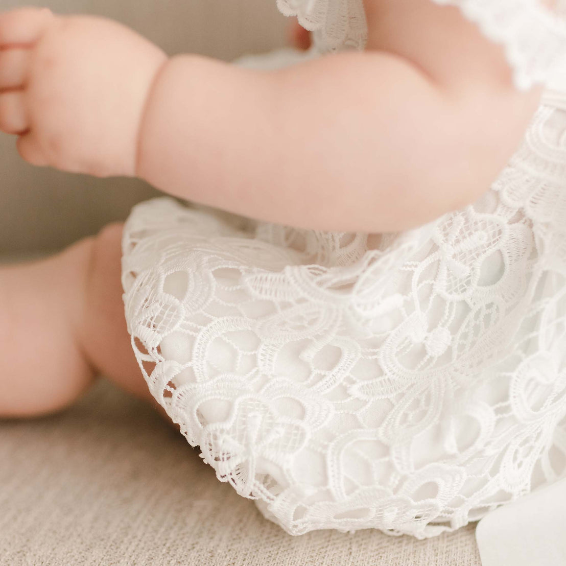 Detail of the Lola Lace Bubble Romper worn by a baby girl, featuring intricate light ivory floral lace and a soft cotton lining.