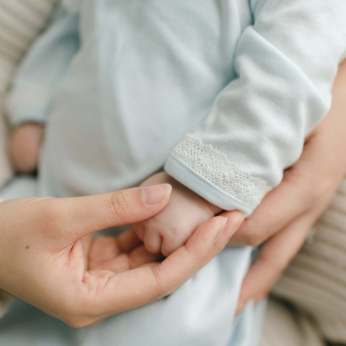 Close up of baby's hand at sleeve cuff of newborn layette