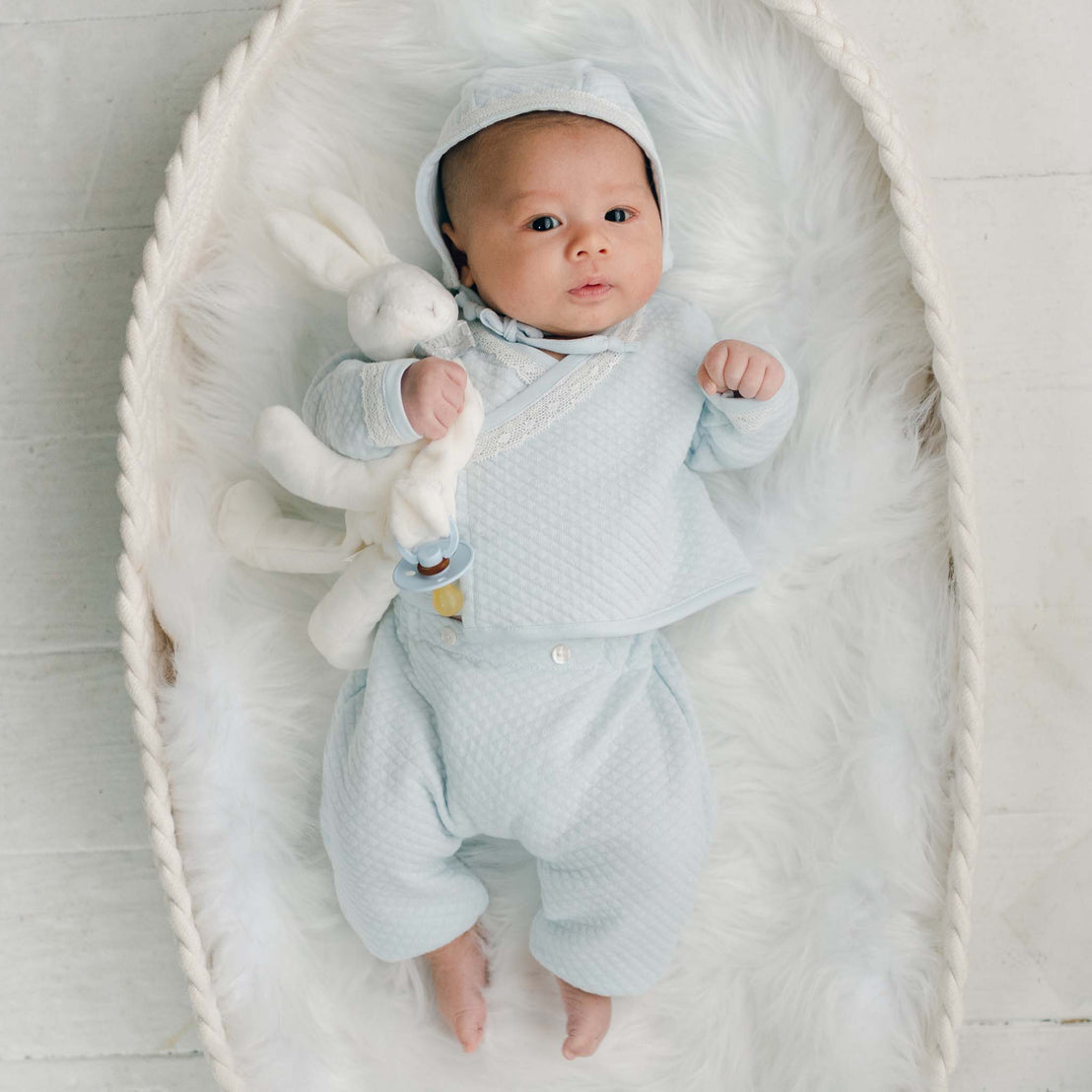 Baby boy blue cotton wrap top, pants and bonnet with bunny laying in basked