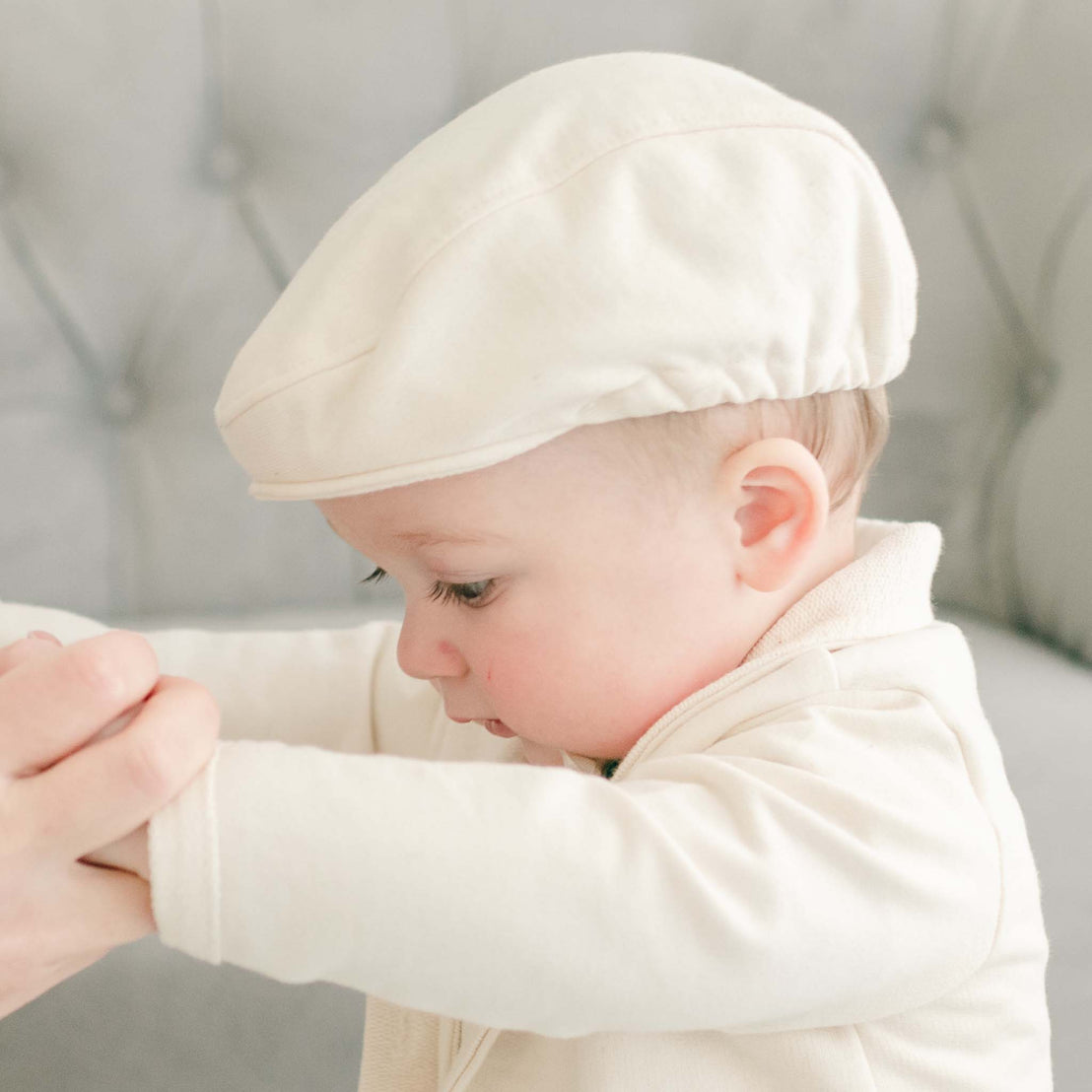 Closer detail of baby boy being guided by his mother. He is wearing the Ezra Tan 4-Piece Suit with matching newsboy cap