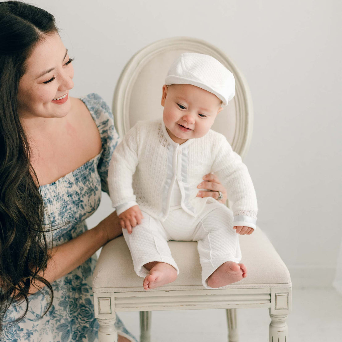 Baby boy sitting on a chair with his mother nearby. He is wearing the Owen 3-Piece Suit, including the sweater, pants, and onesie