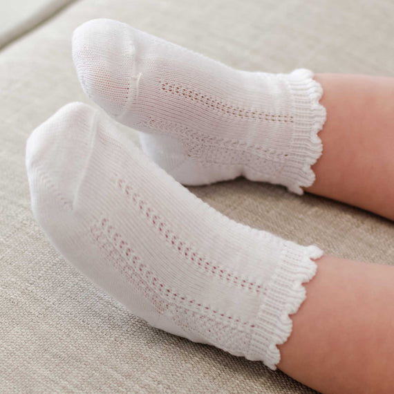 A close-up of a person's feet dressed in white, cotton Pattern Socks, resting comfortably on a cream-colored carpet. The socks feature a delicate, breathable mesh design along the ankles.