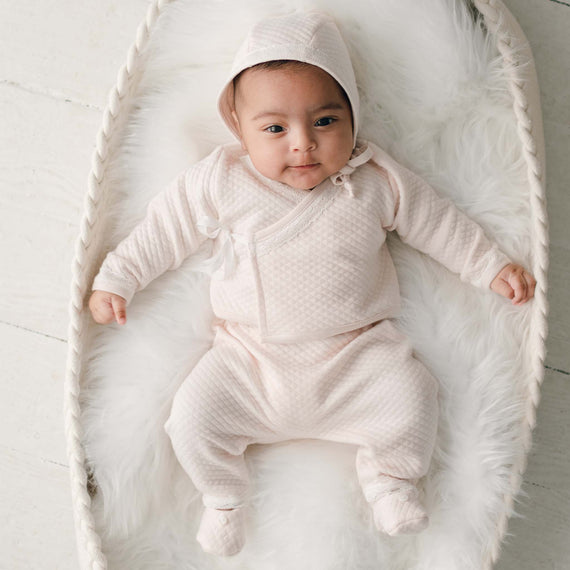 Baby girl in pink cotton wrap top and quilt pants with bonnet and booties in basket