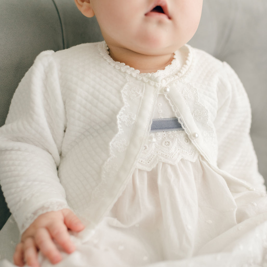 Close up detail shows the Emily Quilted Cotton Sweater's light ivory floral lace trim and white velvet ribbon with pearl style buttons.