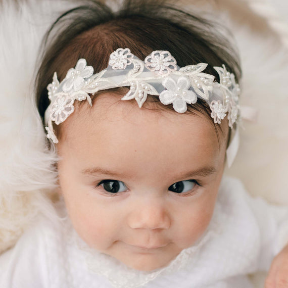 Newborn baby girl wearing the Tessa Flower Headband. The headband is accented with beautiful pink and white floral appliqué and a pink silk ribbon bow.