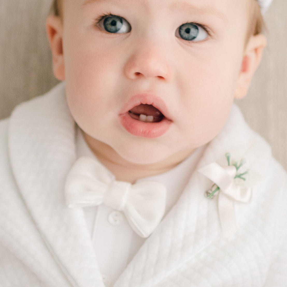 Baby boy wearing a White Velvet Bow Tie and Boutonniere that is attached to his suit